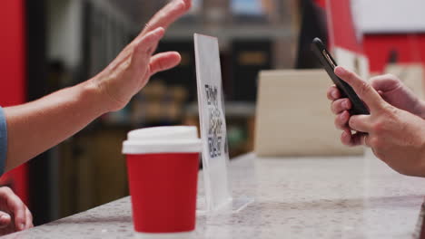 Mid-section-of-woman-scanning-qr-code-with-smartphone-to-make-payment-at-a-cafe