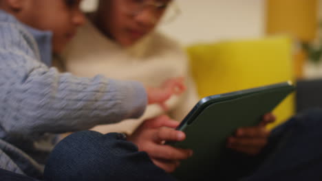 two young boys sitting on sofa at home playing games or streaming onto digital tablet 6