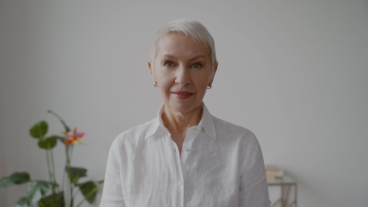 mujer mayor con pelo blanco corto y camisa blanca mirando a la cámara con expresión seria