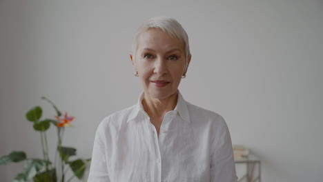 mujer mayor con pelo blanco corto y camisa blanca mirando a la cámara con expresión seria