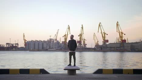 stilvoller hipster-mann auf dem hintergrund des seehafens bei sonnenuntergang, zur seite schauend