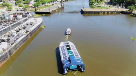 Overhead-view-of-ocean-cleanup-ship-Interceptor-004-on-Ozama-river-being-pulled-by-tug-boat-in-narrow-harbor-port-in-downtown-Santo-Domingo,-Dominican-Republic,-above-aerial-static