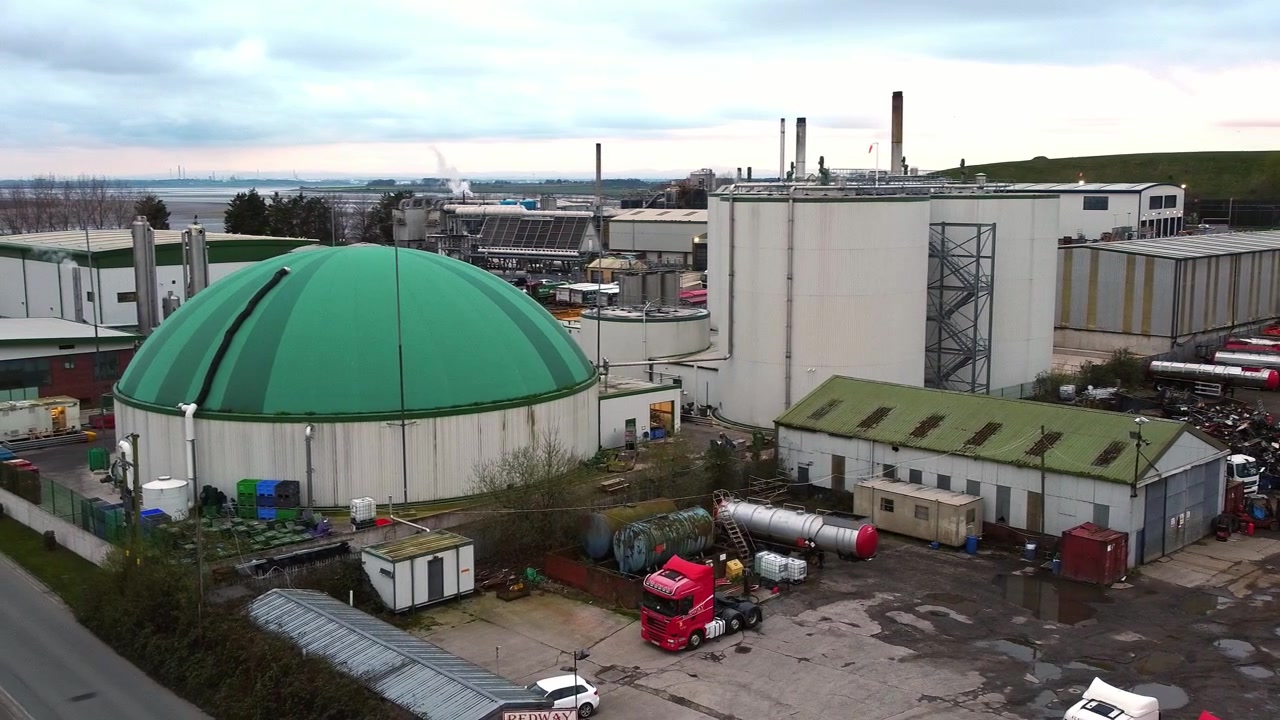 Luftoptagelse i kredsløb mod højre af et industrielt, grønt, kuppelformet siloanlæg til bionedbrydelig genanvendelse af madaffald, lavvinkeloptagelse