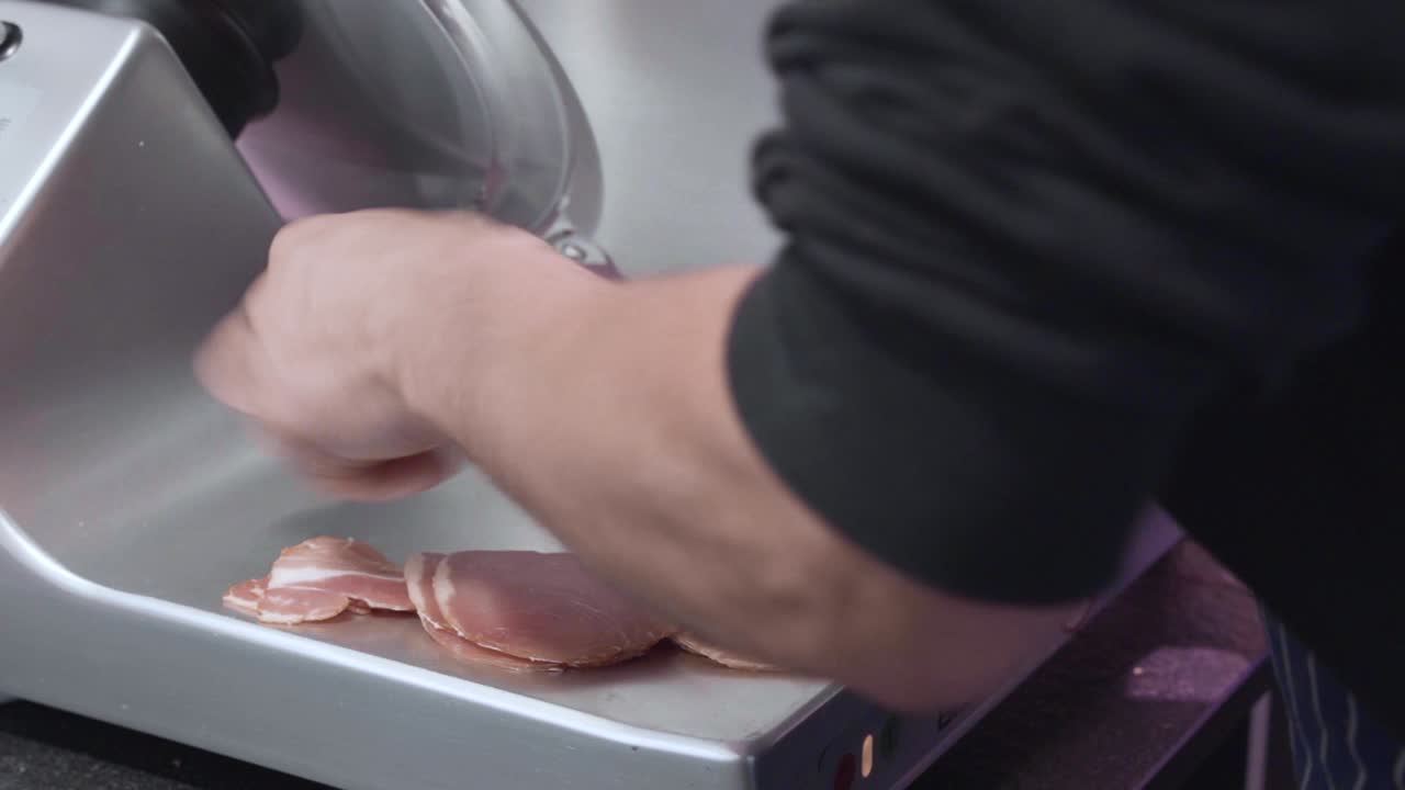 un lavoratore di gastronomia maschio caucasico affetta diversi tipi di carne usando un cutter industriale
