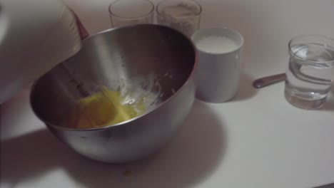 mixing eggs with sugar in stainless steel bowl for pancake batter - ingredients on table for recipe