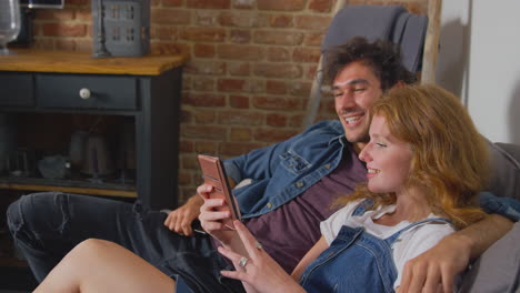 couple sitting on sofa in lounge at home looking at their mobile phone together