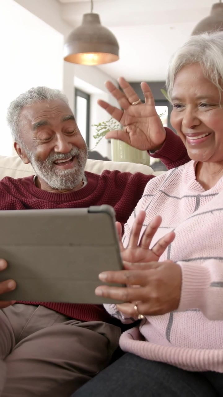 Video verticale: Coppia anziana che saluta giocosamente un tablet sul divano, generando emoji in AR, e poi si sistema.