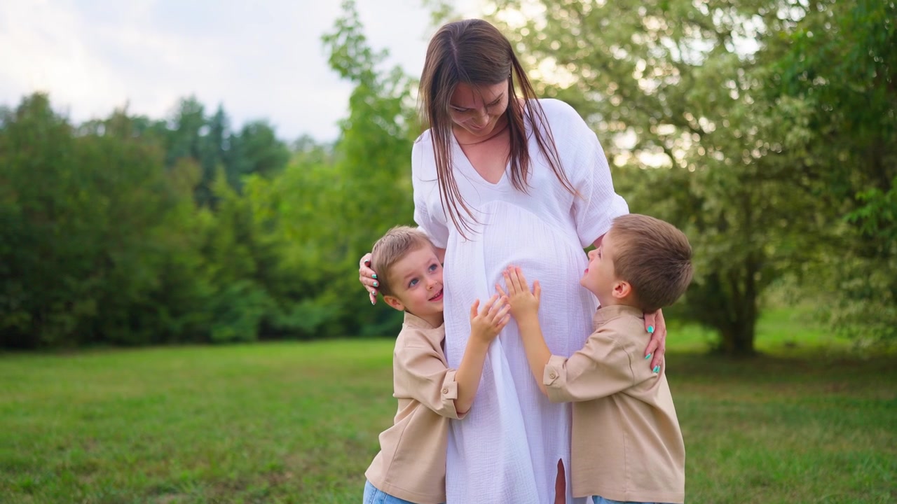 Zwei kleine Jungen umarmen und berühren den Bauch ihrer schwangeren Mutter.