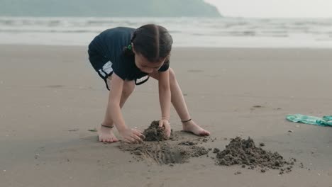 a young girl is having a fun day at the beach, playing and scooping sand with her hands