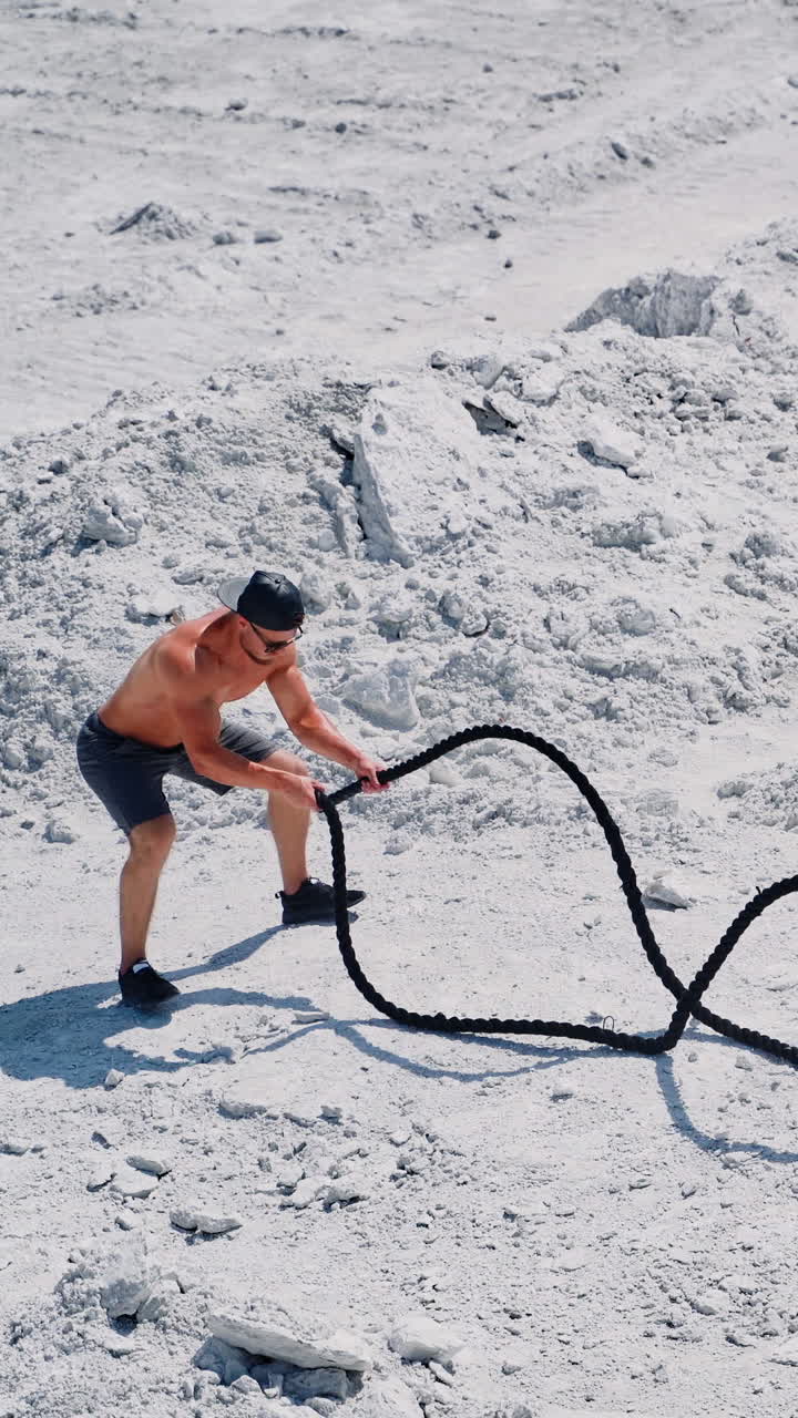 Athletic young man working out with battle ropes. Bodybuilder posing outdoors. Vertical video