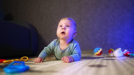 adorable caucasian baby boy with big blue eyes lies on the floor on his belly. lovely infant looking up with surprise and smiling.