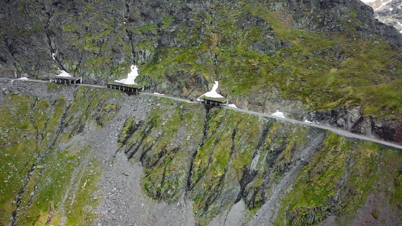 Drone aerial view over Transfăgărășan, winding road, Balea lake lodges, rocky cliffs and mountain mist.