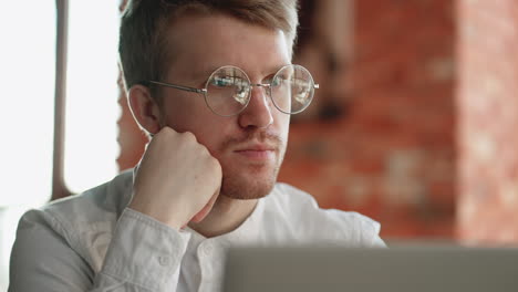 anxious and pensive man is reading news in laptop sitting in cafe closeup portrait of attractive guy with glasses