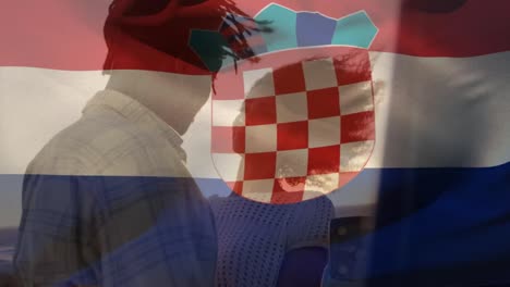 animation of croatia flag waving over happy african american couple embracing at beach