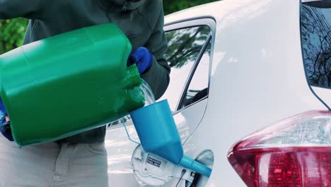 a man pouring gasoline into an empty fuel tank from a plastic red  gas can. filling  the car from the canister into the neck of the fuel tank.