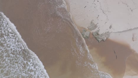 top down drone shot small shorebreak waves breaking on sand and mixing with muddy river sewage runoff in bali indonesia