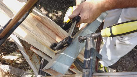 a carpenter works outside with carpenters clamps on timber. he tightens the tool to prevent material shifting. fixes with the fastening devices