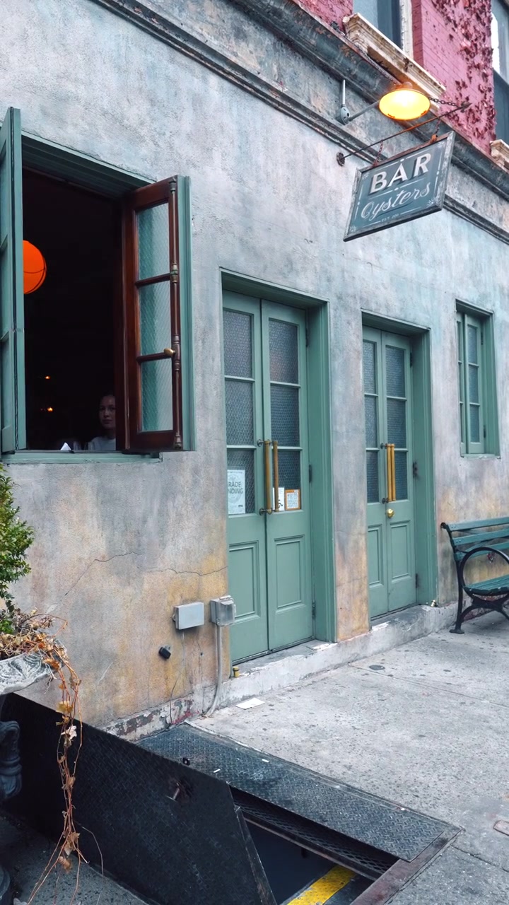 New York, USA, 25 dicembre 2025: Facciata di bar e ristorante di ostriche con porte verdi. Lanterne appese sopra l'ingresso di un edificio rustico con porta della cantina aperta sul marciapiede