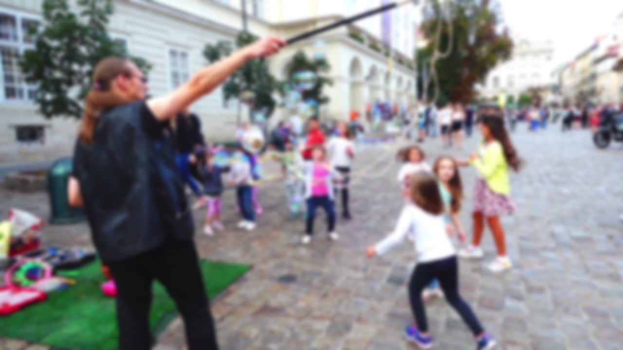 O homem entretém crianças com bolhas de sabão na praça da cidade. Fora de foco.