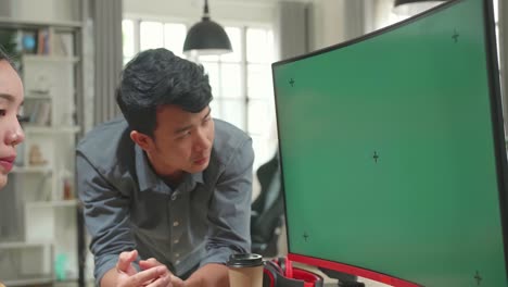 asian female arguing with her male colleague on a project on her personal computer with mock-up green screen. they work in a creative loft office