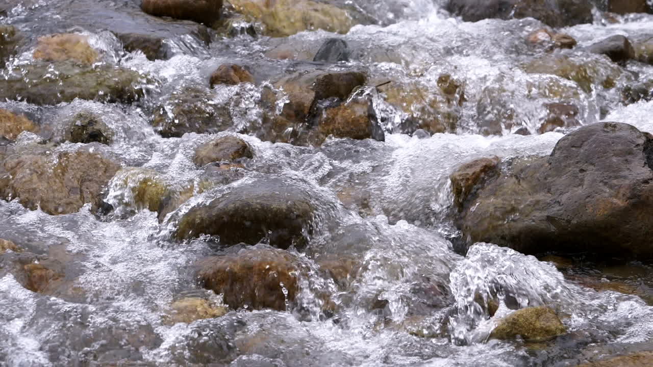 Riacho límpido correndo entre pedras. Rio caudaloso fluindo em câmera lenta.