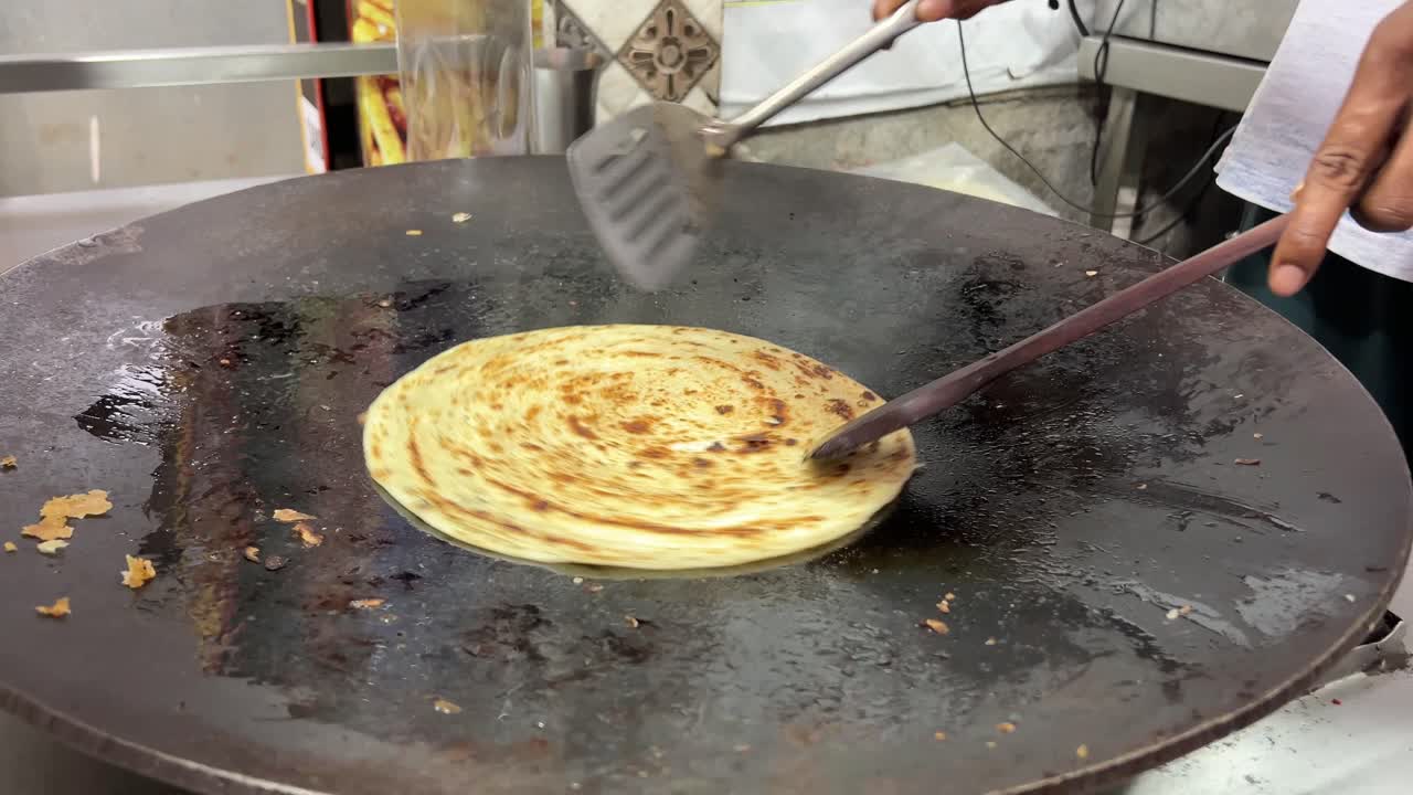 un hombre preparando lacha paratha en una tienda en la india
