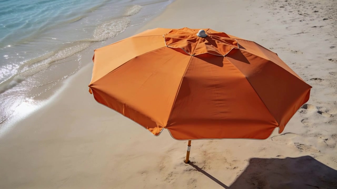 Grande ombrellone da spiaggia arancione in piedi proietta ombra sulla sabbia sulla riva, con onde in arrivo portate dalla marea.