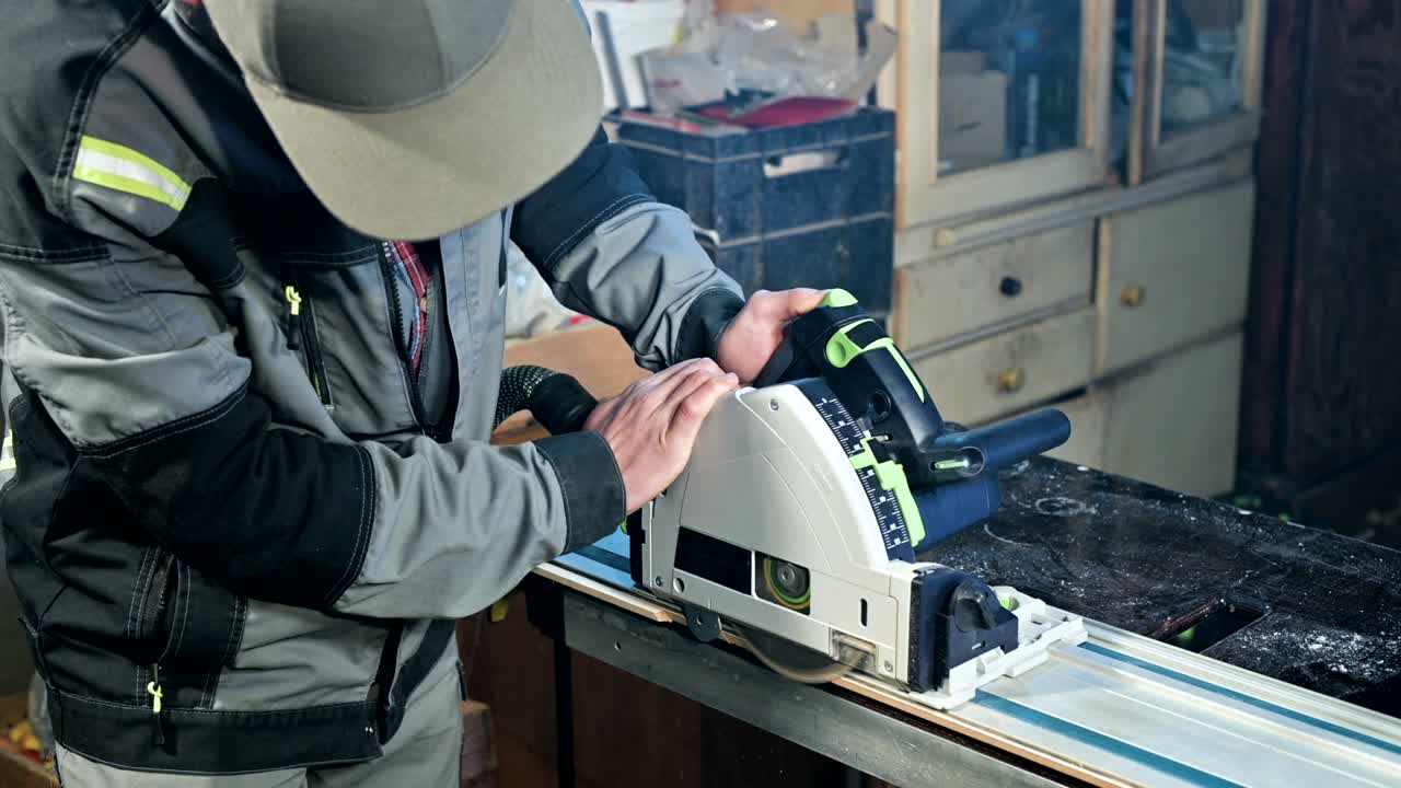 회색 오버을 입은 수염을 가진 젊은 남자가 직업으로 목수입니다. 원형 절단 기계로 일합니다.