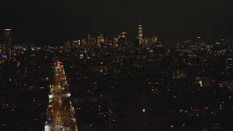 Aerial-descending-footage-of-metropolis-at-night.-Cityscape-with-hundreds-of-lights-and-downtown-skyscrapers-in-background.-Manhattan,-New-York-City,-USA