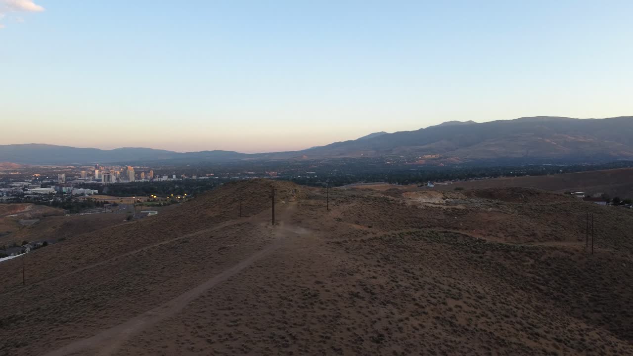 toma aérea de un sendero en una colina del desierto con la puesta de sol en reno y las montañas de sierra nevada en el fondo