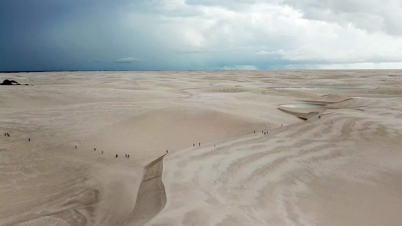 Aerial panorama shot of refugees crossing desert towards forest. Storm on the horizon.