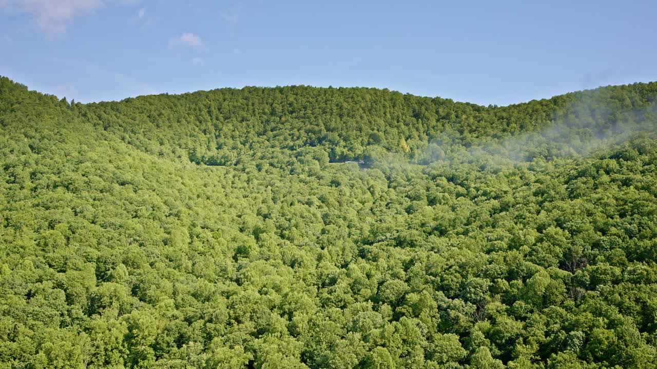 The drone soars above layers of ridges, each softened by the morning’s mist