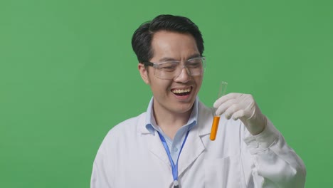 close up of asian man scientist looking at the orange liquid in the test tube and saying wow while standing on the green screen background in the laboratory