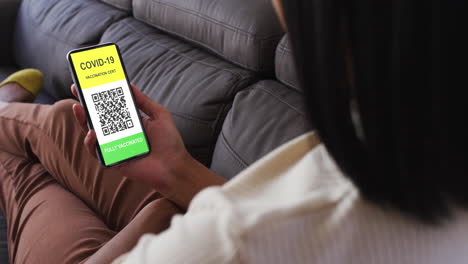 mujer en casa con un teléfono inteligente con certificado de vacunación contra la covid y código qr en la pantalla