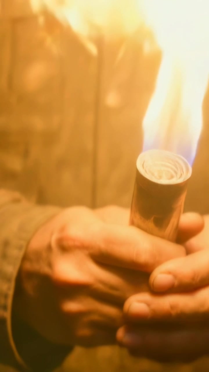 Video verticale: Fiamma che erutta, uomo con cappotto pesante che impugna una torcia e blocca il calore in una stanza fiocamente illuminata.