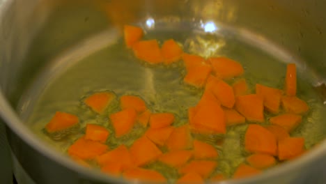 The-cook-tops-fresh-cut-carrots-in-to-the-hot-boiling-olive-oil-in-the-steel-pot,-handheld-close-up-shot