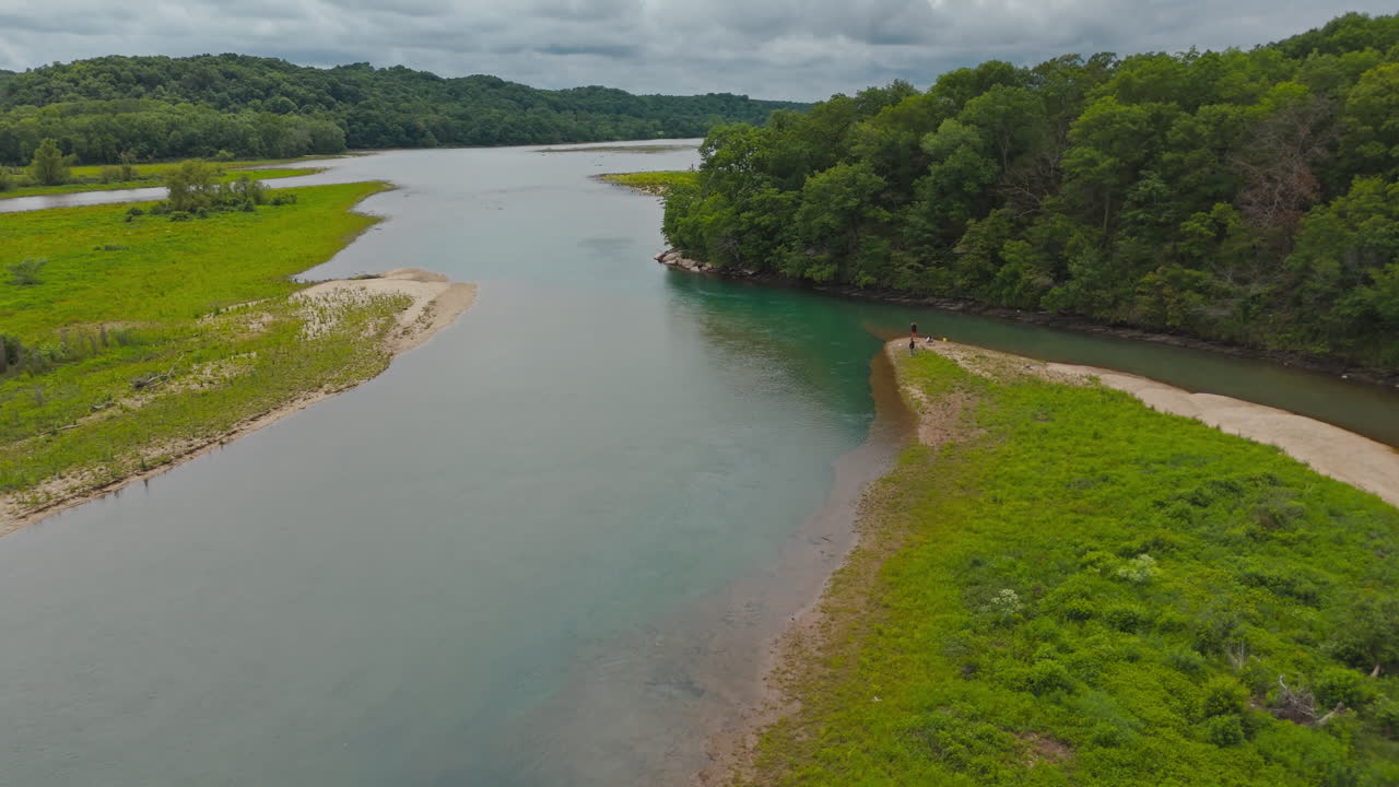 Group of people fishing on quiet lakeside sandy bank near dense green forest under soft daylight, Tagg Flats, Lake Eucha Oklahoma USA, aerial pullback