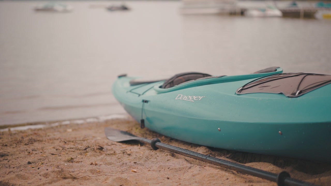 Kayak e pagaia su spiaggia sabbiosa con dolci onde del lago che si infrangono, in condizioni di scarsa illuminazione 4K ProRes.