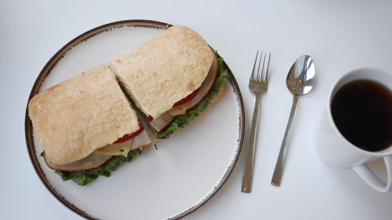 Hand holding a sandwich with coffee on a table