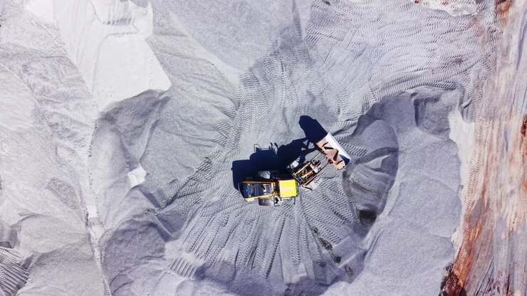 Wheel loader working in gravel quarry. Overhead drone shot shows machine tracks across gray gravel mounds and rocky terrain.