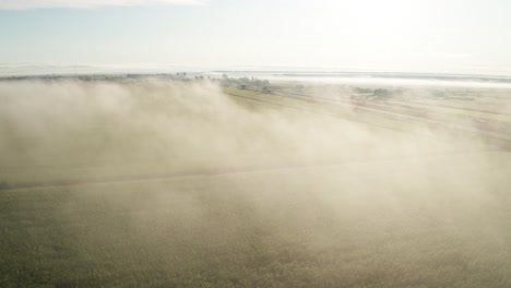 pale blue sky above morning fog hanging over bright green farm field and highway passing through the plains