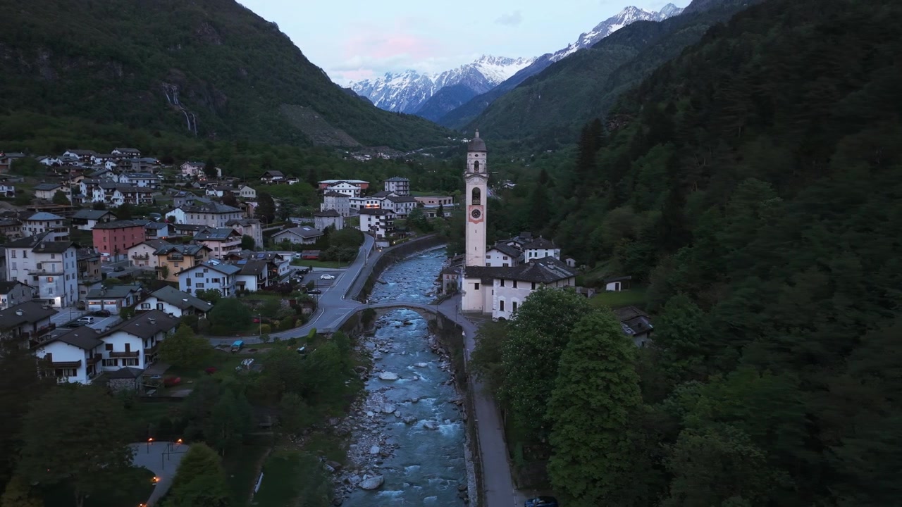 Prospettiva aerea di Piuro, un villaggio alpino incastonato in una valle con un fiume e montagne innevate.