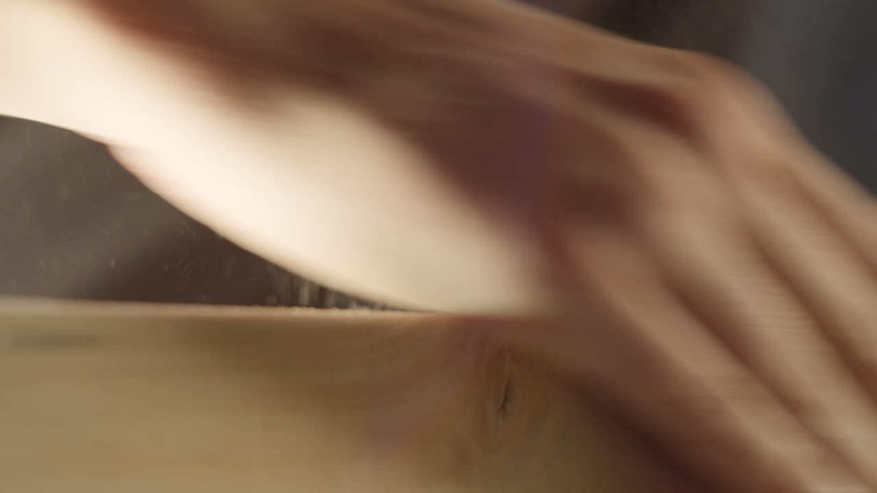 High quality video showing a craftsman sanding a wooden board in warm light with slow smooth hand movements and fine dust in the air creating a rich tactile workshop atmosphere