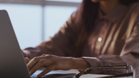 businesswoman working late using laptop at desk in office taking off glasses