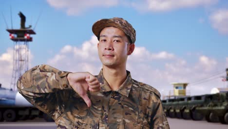 군사 캠프에 서 있는 동안 카메라에 엄지손가락을 내려놓은 아시아인 군인의 클로즈업
