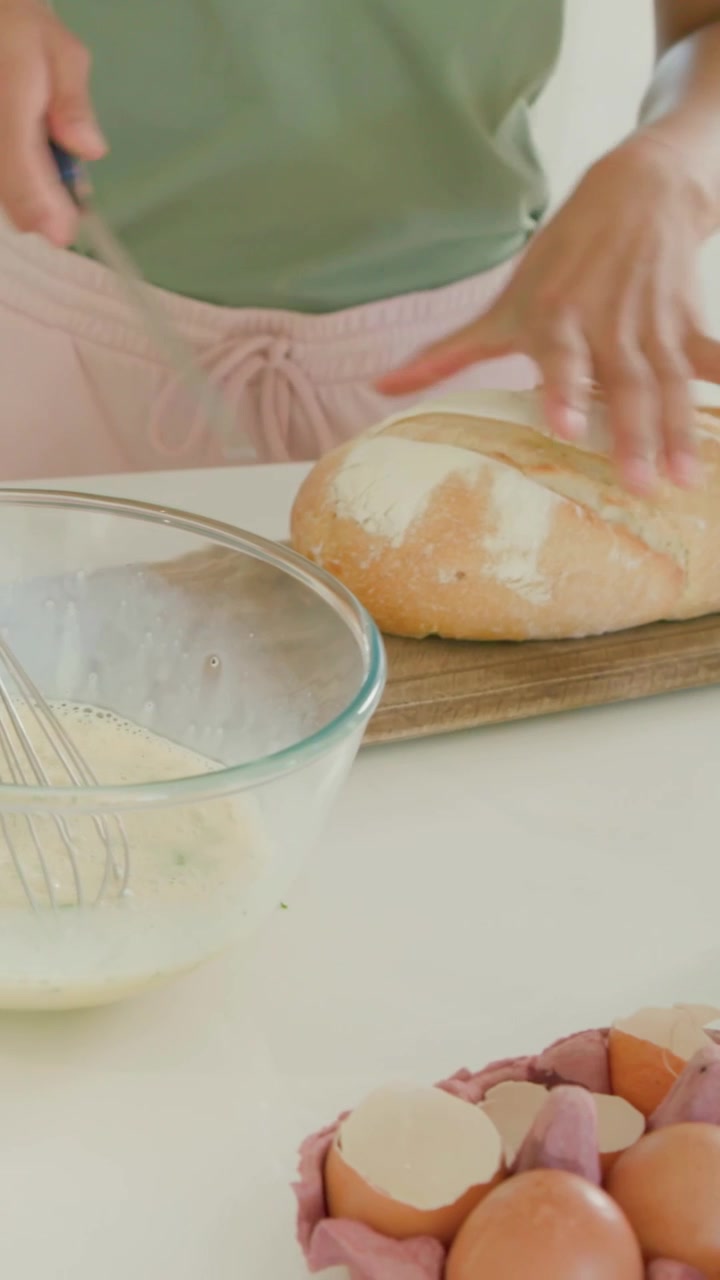 Vertical video: Slicing cook in green top preparing breakfast on counter, with avocado, bread, eggs