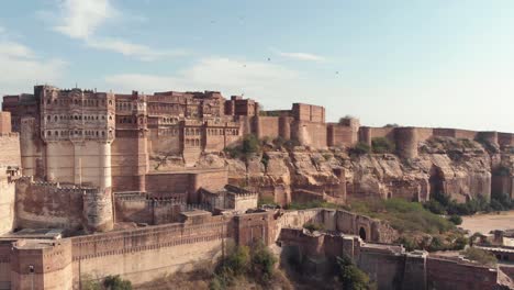 Mehrangarh-Fort-standing-above-the-sky-line-of-Jodhpur,-Rajasthan,-India---Aerial-Panoramic-Orbit-shot