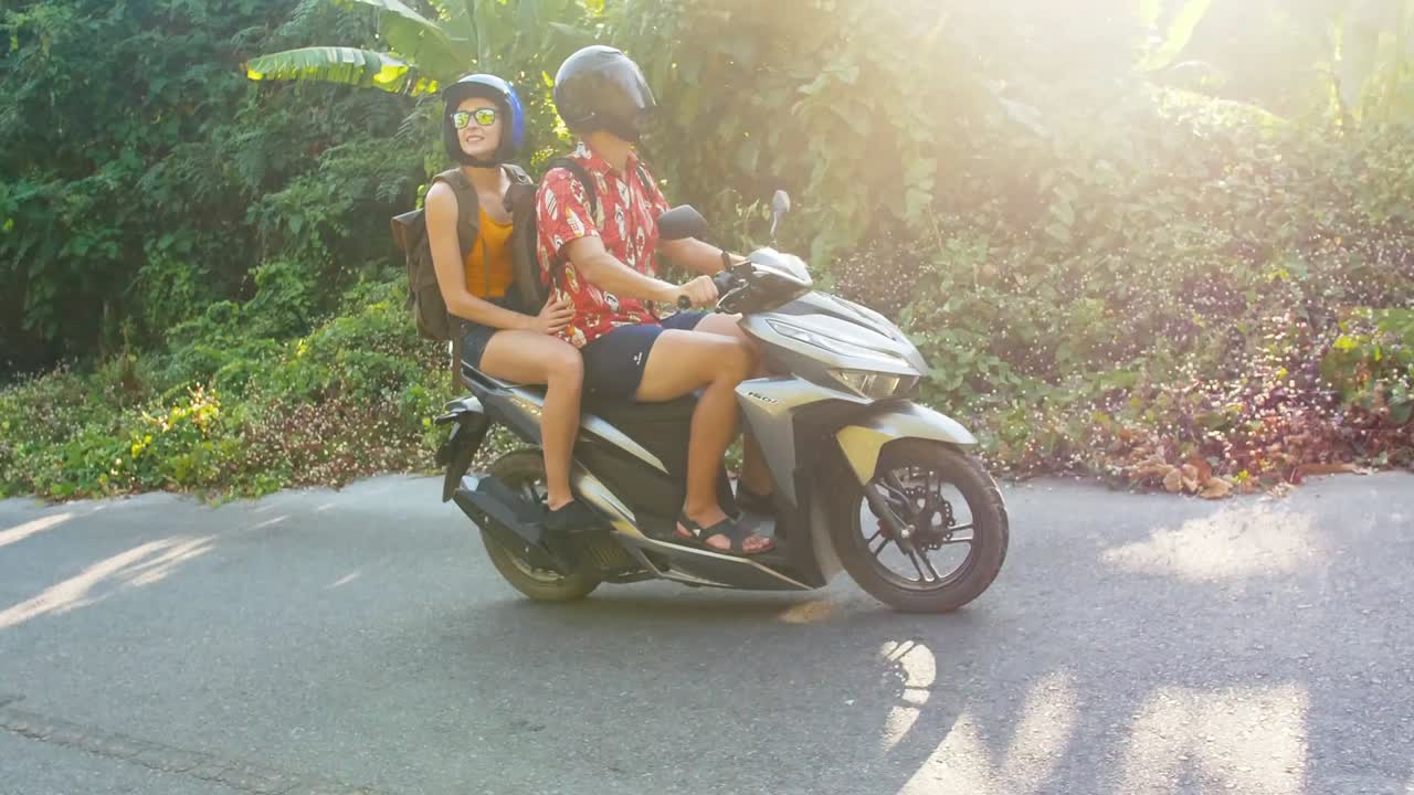 아름다운 젊은 관광 부부는 헬을 착용한 스쿠터를 타고 정글을 여행합니다. 여행, 자유, 행복, 휴가, 신혼여행 개념.