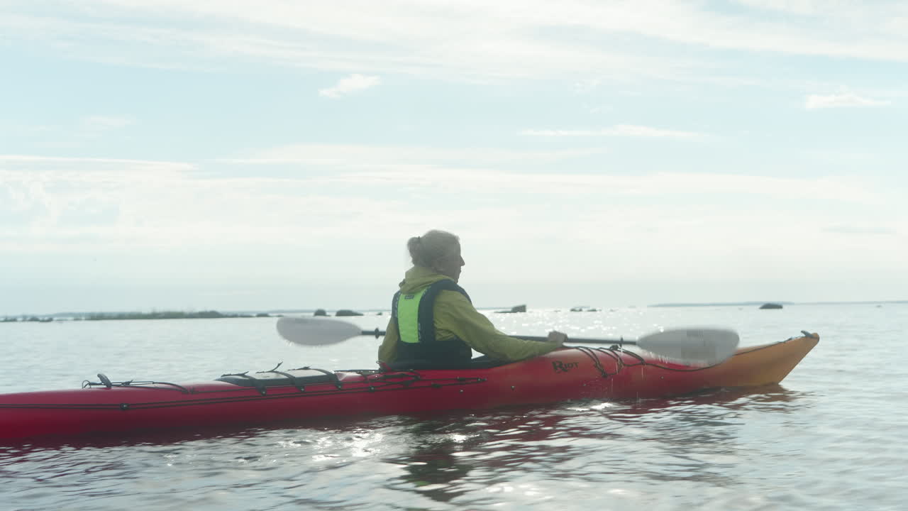 joven mujer rubia remando en un kayak del mar rojo en el mar abierto en finlandia, vaasa, archipiélago, hermosa atmósfera de atardecer de verano, primer plano