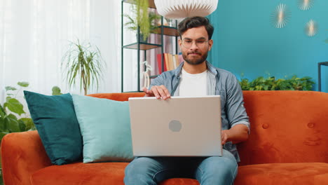 Junger-Freiberuflicher-Mann-Sitzt-Auf-Der-Couch-In-Der-Nähe-Eines-Laptop-PCs,-Nachdem-Er-Die-Arbeit-Im-Wohnzimmer-Zu-Hause-Beendet-Hat